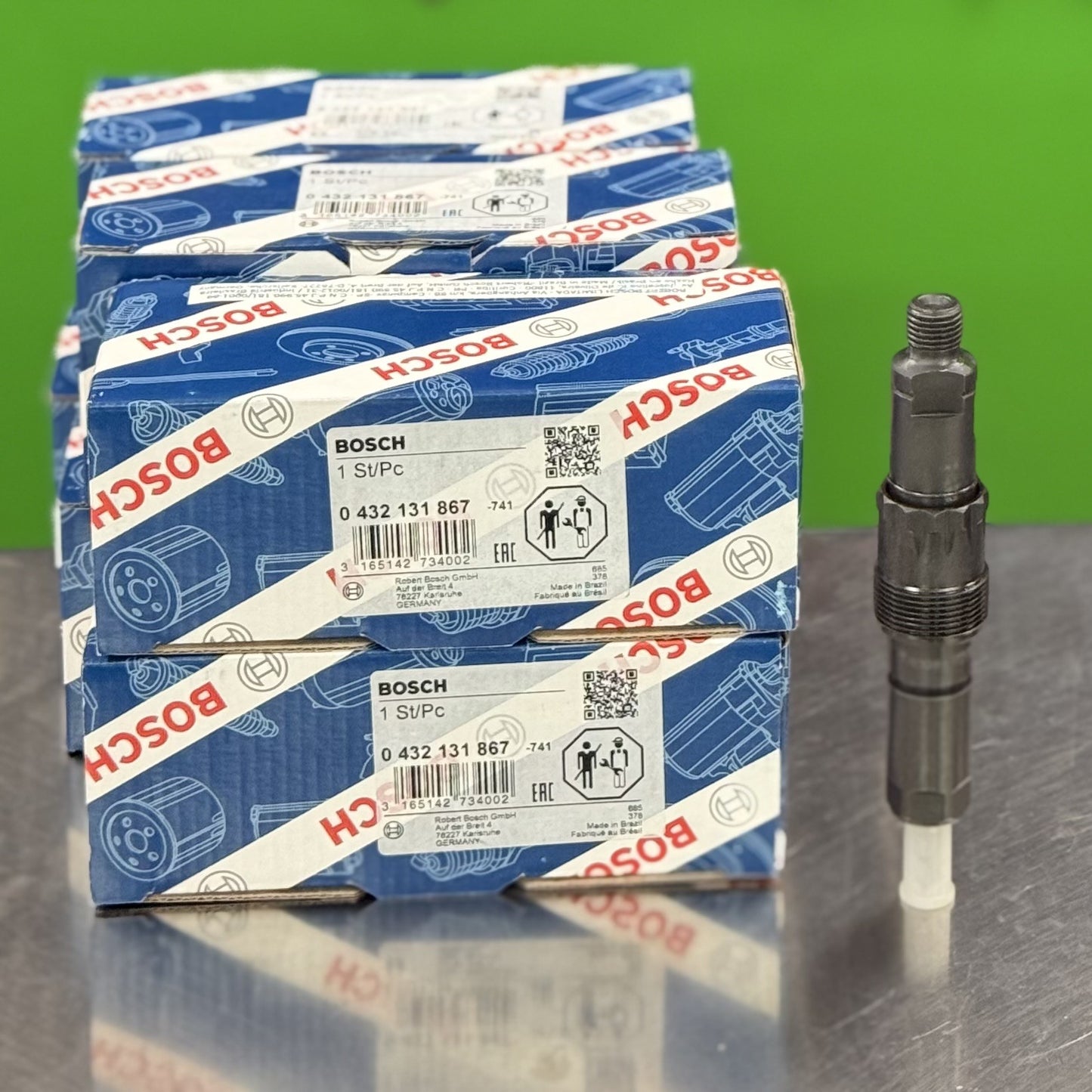 Stack of Bosch branded boxes with a spark plug on a reflective surface and green background